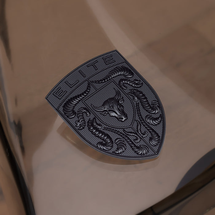A dark metallic porsche badge featuring an embossed brahma bull head and the word 'ELITE' at the top, displayed on a reflective beige surface.