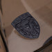 A dark metallic porsche badge featuring an embossed brahma bull head and the word 'ELITE' at the top, displayed on a reflective beige surface.