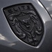 A close-up of a black porsche shield emblem on a dark metallic gray vehicle surface, featuring the word ELITE at the top and a bull head in the center.