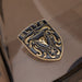 A close-up of a metallic porsche badge or emblem with the word "ELITE" at the top, featuring a stylized bull head and crumrine designs in polished gold-toned metal over a dark textured background.