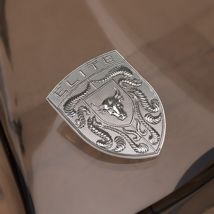 A Chrome Silver Brahma Bull Hood Emblem with an engraved bull design and the word 'ELITE' at the top, resting on a glossy brown surface.