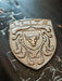 A metallic bronze shield-shaped porsche badge featuring a central bull head crest and the word 'ELITE' at the top, resting on a dark textured surface.