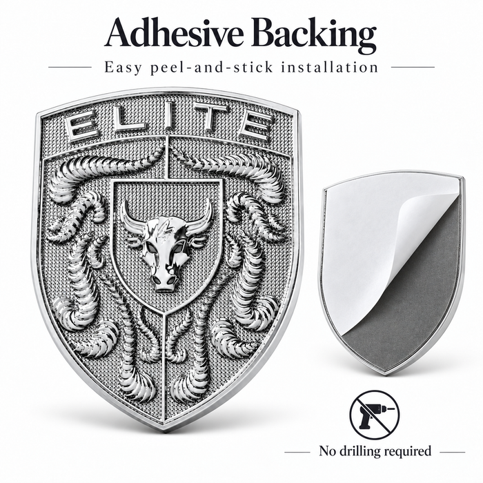 A silver metallic shield-shaped porsche badge with an embossed bull crest and the word 'ELITE' at the top, shown alongside a smaller view of its peel-and-stick backing. Text at the top reads 'Adhesive Backing' and 'Easy peel-and-stick installation,' with a 'No drilling required' icon at the bottom.