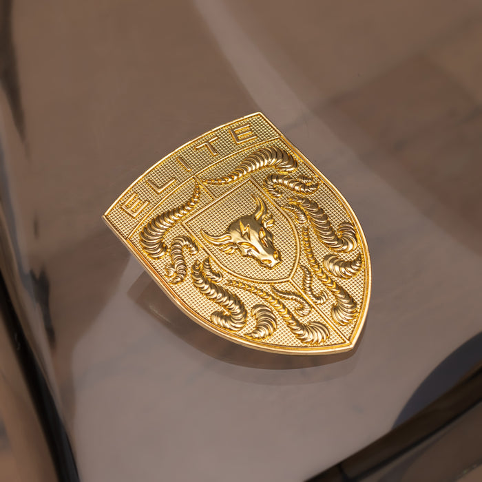 A gold metallic porsche badge with an embossed bull head and the word 'ELITE' on a glossy reflective surface.