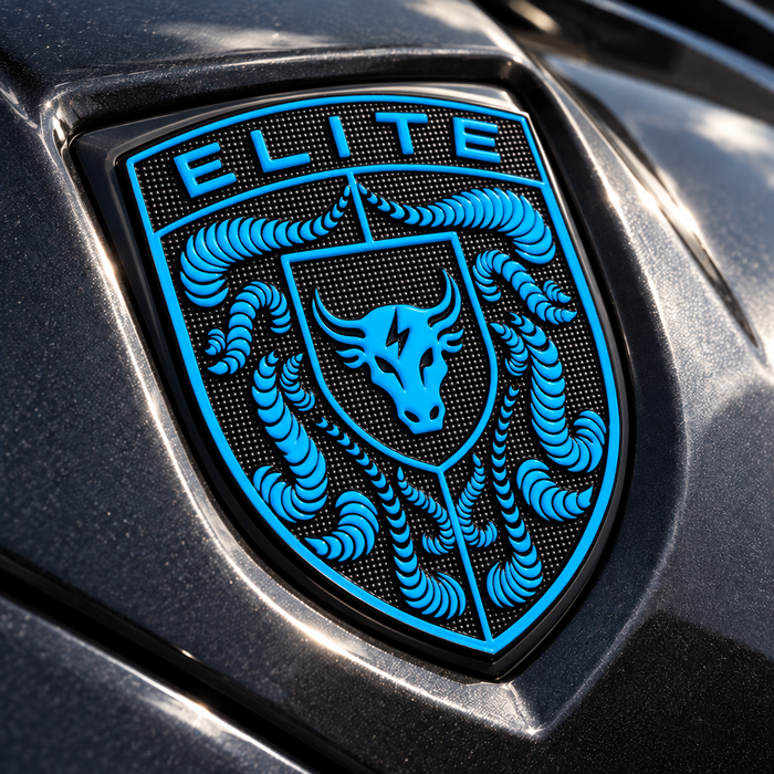 A close-up of a glossy black Porsche Mexico Blue Brahma Bull Hood Emblem featuring a bright blue shield design with a bull head, crumrine designs, and the word "ELITE" at the top, mounted on a dark metallic vehicle surface.