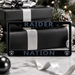 A black license plate frame with 'RAIDER NATION' in dark blue lettering and small Raiders logos in the corners, shown in a holiday gift setting with wrapped presents and pinecones.