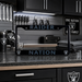 A black license plate frame with light blue Raiders branding and the words 'RAIDER NATION' is displayed on a dark kitchen counter. The background shows a matching Raiders-themed kitchen with a helmet, towel, and sign.