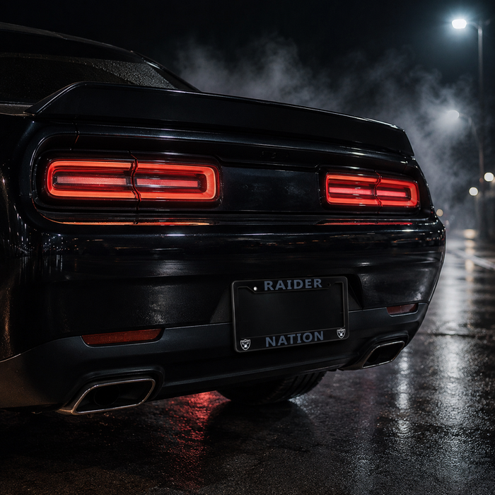 Rear view of a black muscle car on a wet night street, with illuminated red taillights and a custom license plate reading 'RAIDER NATION'.