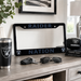 A black license plate frame with 'RAIDER NATION' in blue lettering and Raiders logos, displayed on a wooden console table in a living room setting alongside a Raiders tumbler, sunglasses, keys, and a football.
