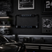 A black license plate frame with 'RAIDER NATION' and Oakland Raiders logos, displayed in a dark, modern room with framed sports memorabilia, a helmet on a shelf, and a car hood in the foreground.