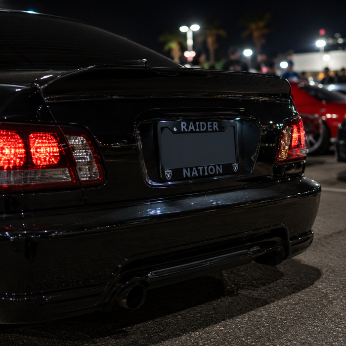 Rear view of a glossy black car at night with a custom license plate frame reading 'RAIDER NATION'.