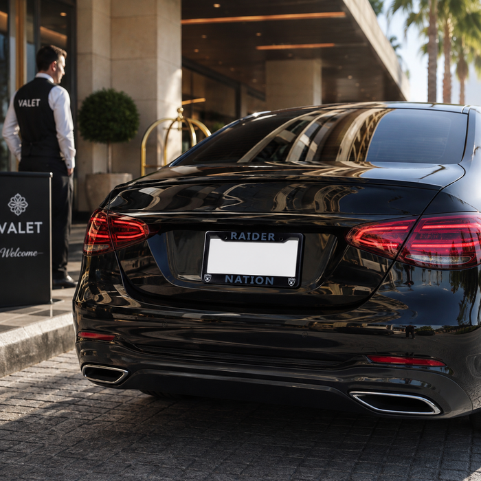 A glossy black luxury sedan parked outside a hotel or valet stand, shown from the rear. The license plate frame reads 'RAIDER NATION'.