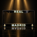 A black license plate frame featuring 'REAL MADRID' in gold and white lettering, with the Real Madrid crest in the corners, set against a dark background with dramatic golden spotlights.
