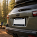 A close-up rear view of a dark olive SUV parked outdoors in a wooded setting, showing a custom license plate frame with 'SEATTLE' at the top and 'SEAHAWKS' with team logos at the bottom.