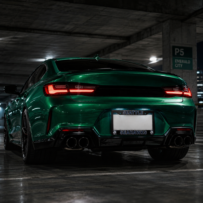 A glossy metallic green sports coupe photographed from the rear in an indoor parking structure. The car has black trim, dual exhaust pipes, and a license plate frame with the word "SEAMAWKS" visible.