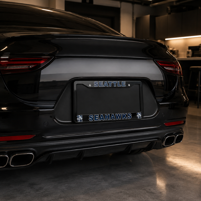 A black Porsche rear bumper and trunk area with a custom black license plate frame reading "SEAHAWKS" and "SEATTLE" in blue lettering, photographed in a garage setting.