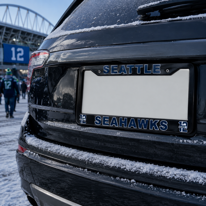 A black license plate frame with 'SEATTLE' on the top bar and 'SEAHAWKS' on the bottom bar, mounted on the rear of a black SUV in the snow near a stadium.