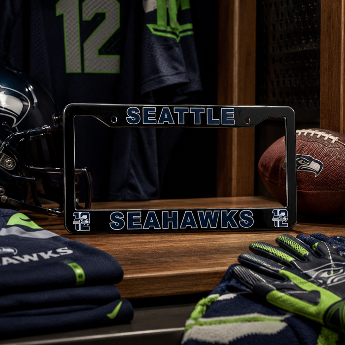 A black Seattle Seahawks license plate frame displayed on a wooden shelf in a locker room setting, surrounded by Seahawks gear including a helmet, folded jerseys, gloves, and a football.