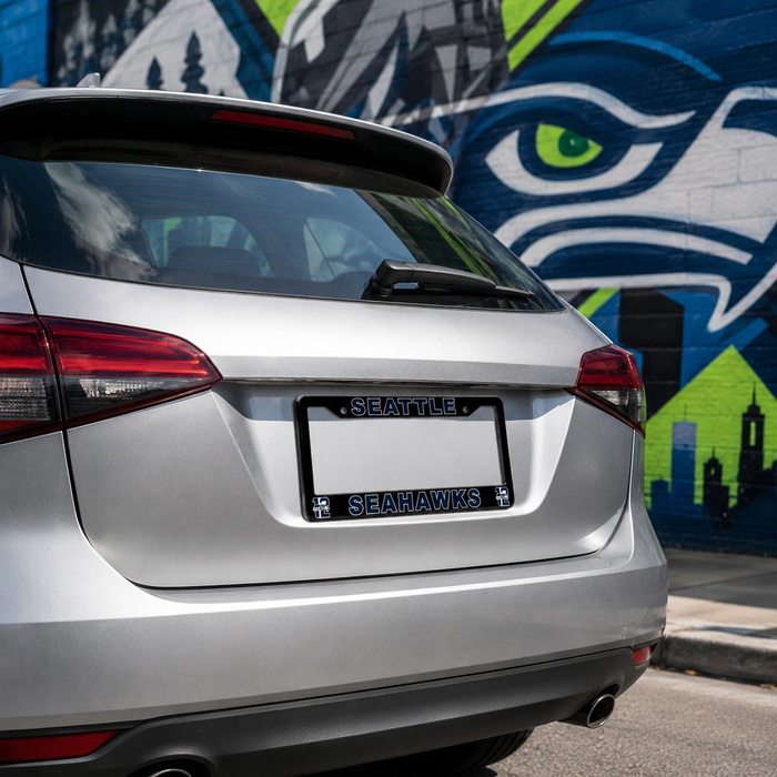 A silver SUV shown from the rear, featuring a custom black license plate frame with 'SEATTLE' and 'SEAHAWKS' text and team logos. The car is parked in front of a colorful Seattle Seahawks-themed brick wall mural.