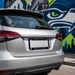 A silver SUV shown from the rear, featuring a custom black license plate frame with 'SEATTLE' and 'SEAHAWKS' text and team logos. The car is parked in front of a colorful Seattle Seahawks-themed brick wall mural.