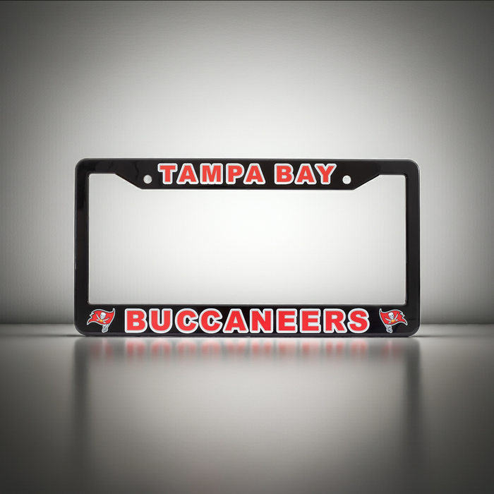 A black license plate frame featuring 'TAMPA BAY BUCCANEERS' in red and white lettering, with the Tampa Bay Buccaneers logo on the bottom corners, shown on a reflective gray surface.